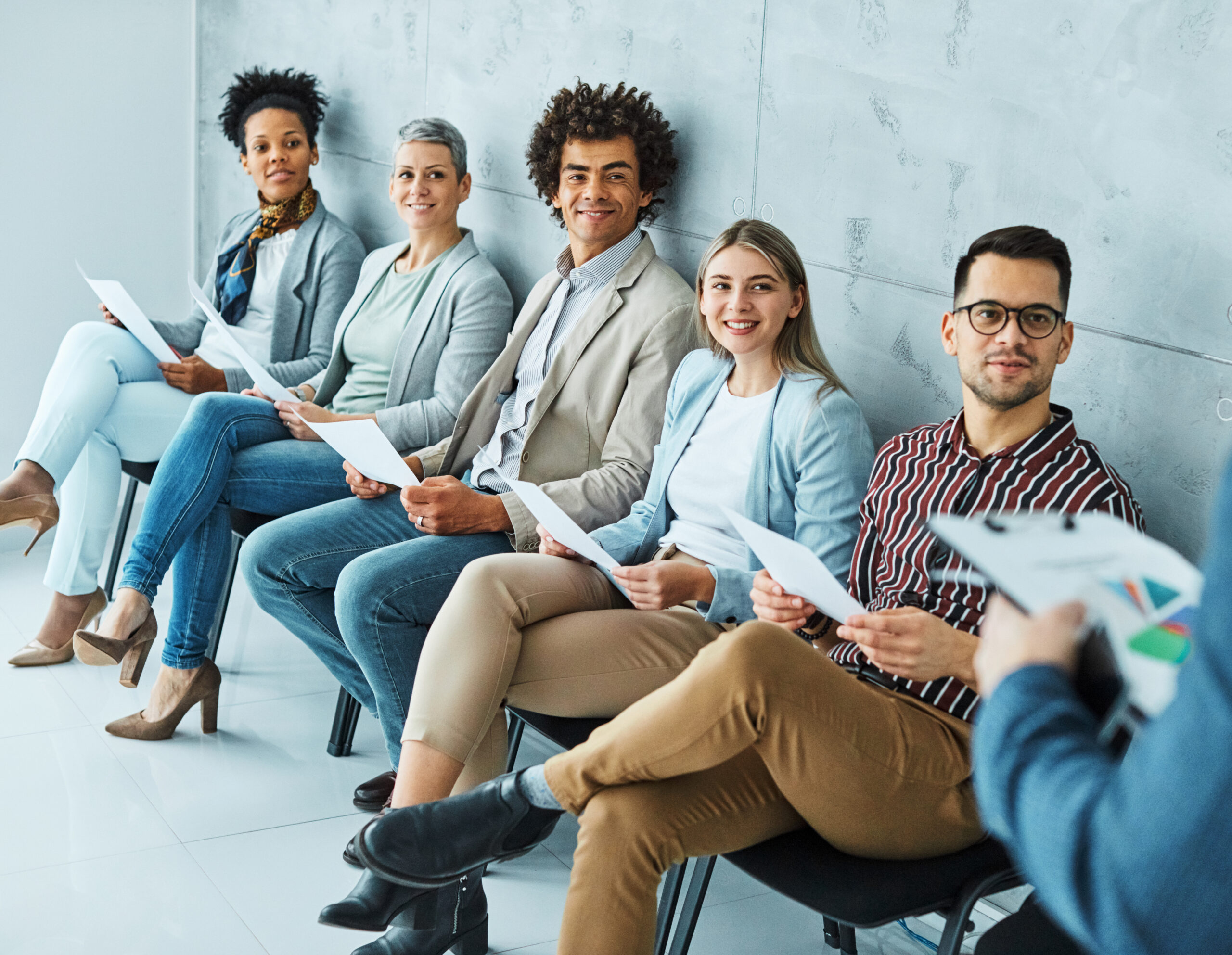Professionals sit in a row, holding papers while waiting to be called for an entry level job interview.
